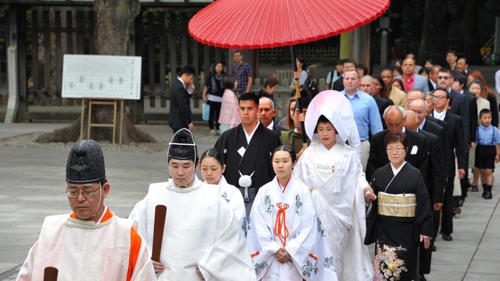 @The Japan Times: Jonathan Madrid, 24, and Nao Sasaki, 30, are led by priests to the wedding hall …