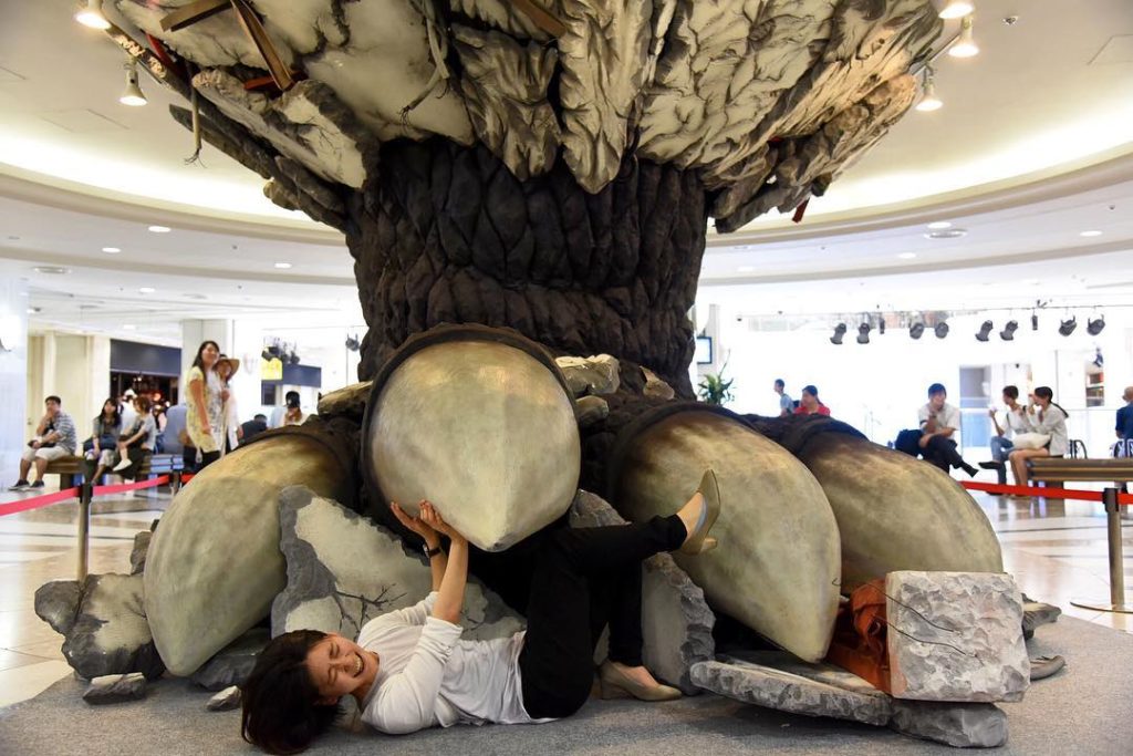 @The Japan Times: A woman lies under a mock Godzilla foot set up at the Namja Town amusement park …
