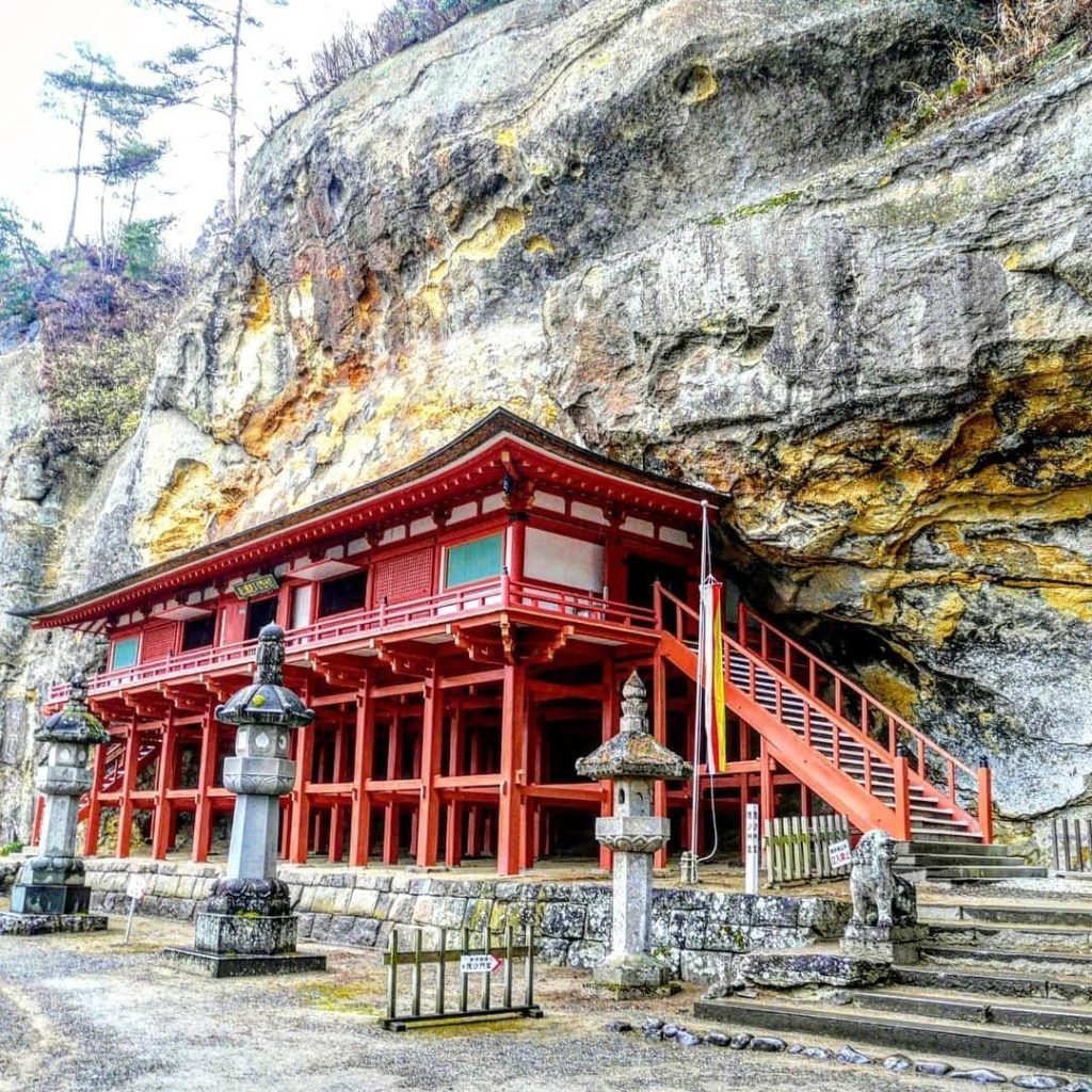 A cave of secret relics buried in a sheer cliff with a temple built against the ...