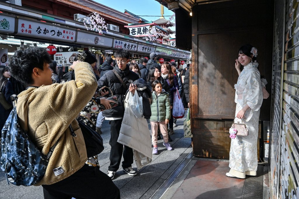 A woman (R) wearing a kimono poses for photos along the main shopping street at Sensoji Temple in the popular tourist destination of Asakusa in central Tokyo on February 21, 2025.