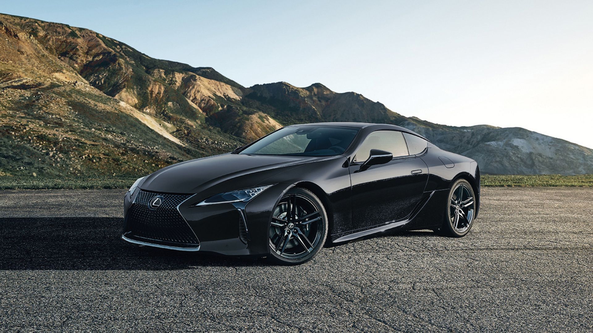 Front three-quarter view of a black 2025 Lexus LC parked on gravel with mountains in the background.