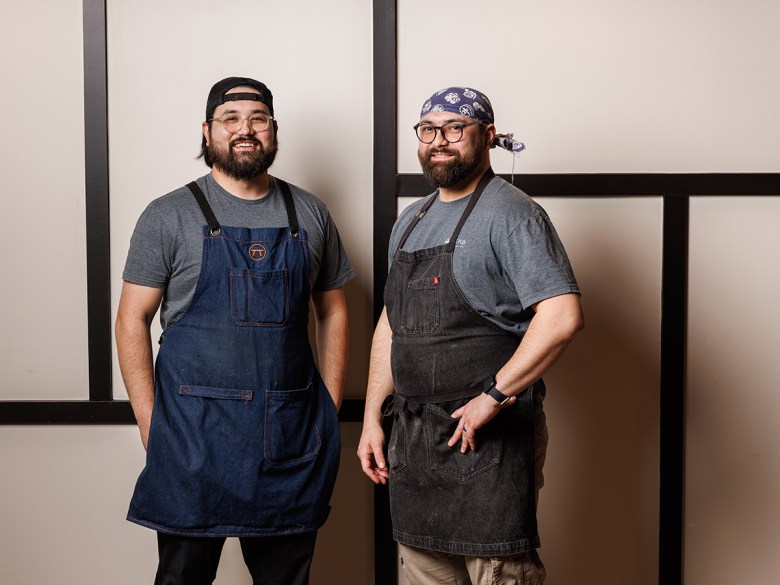 Two men wearing denim aprons pose at Mt. Fuji.