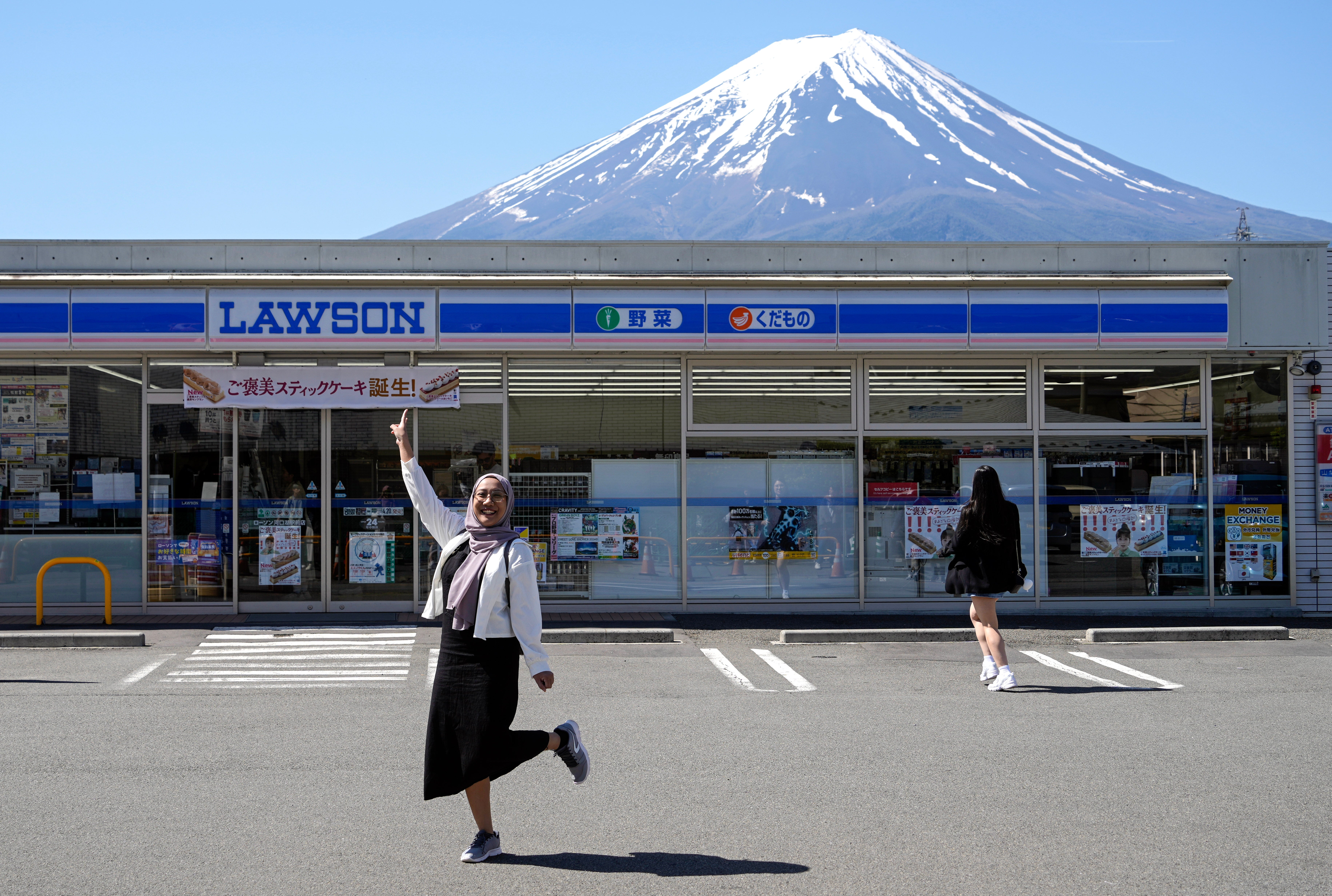 A foreign tourist poses in front of the Lawson Kawaguchiko Ekimae convenience store