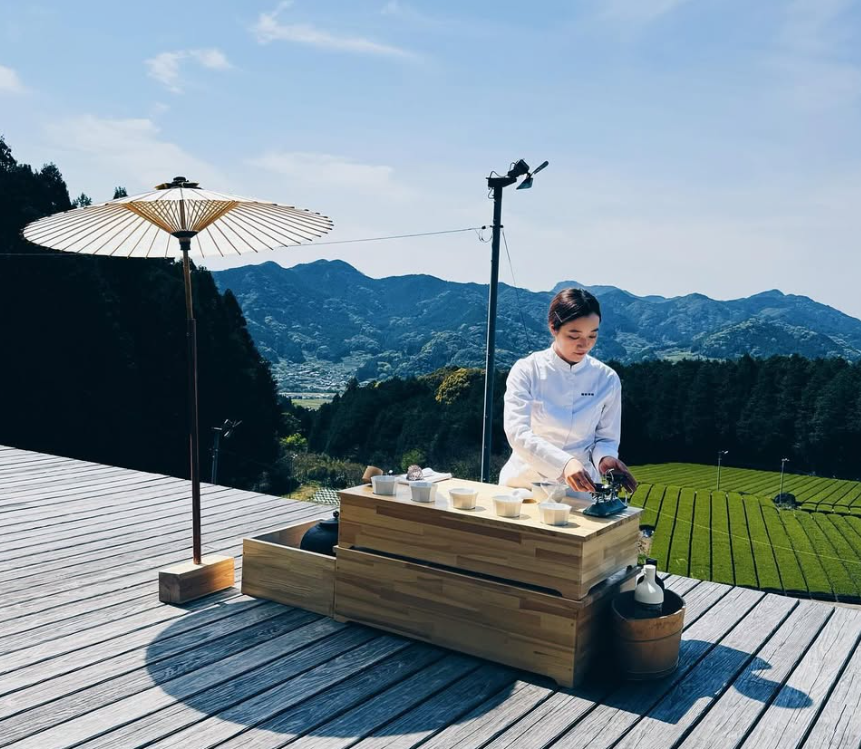 A Japanese chef prepares culinary delights on a deck with greenery and mountains looming in the background