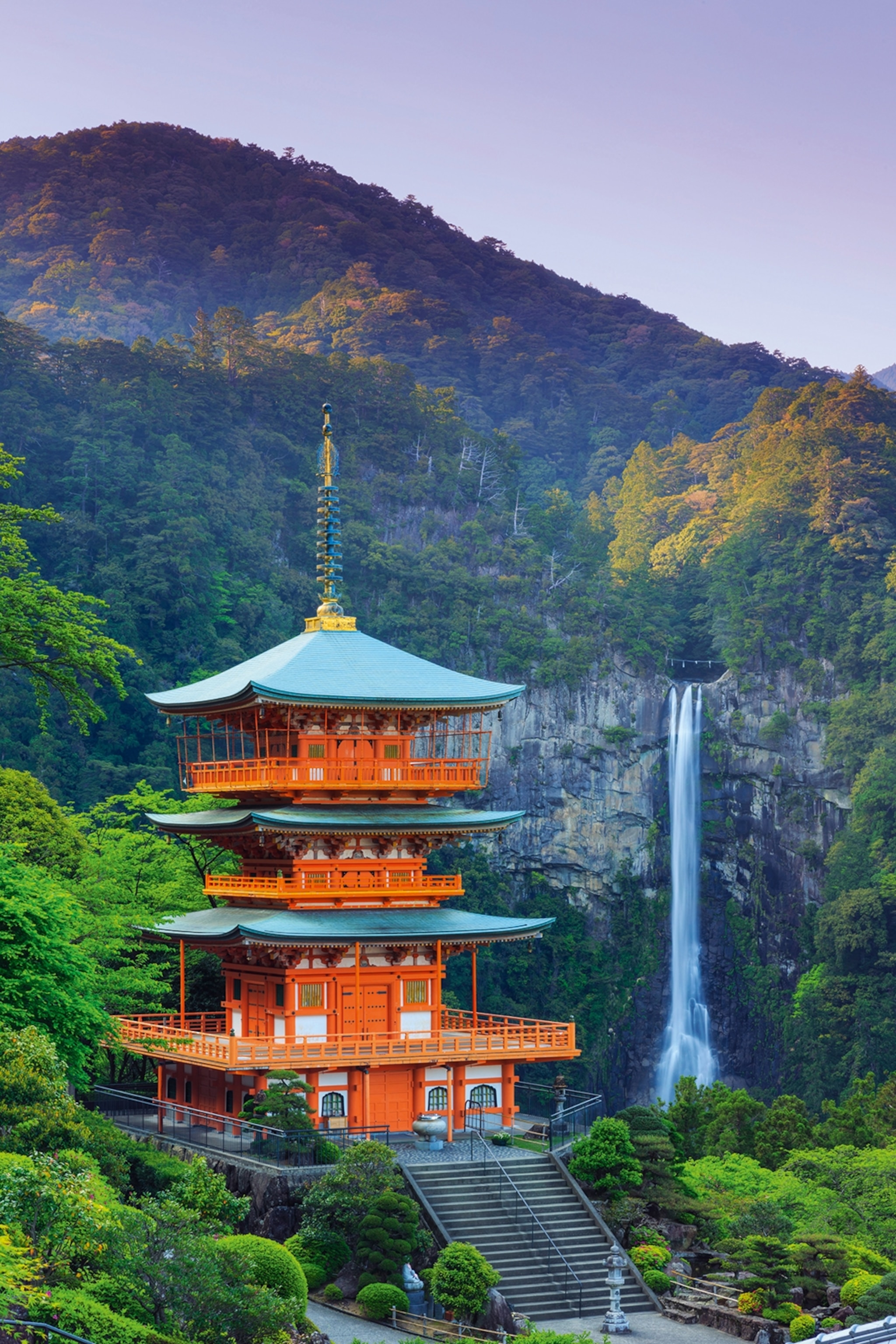 Red pagoda tiered temple stood against a waterfall in mountainous terrain.
