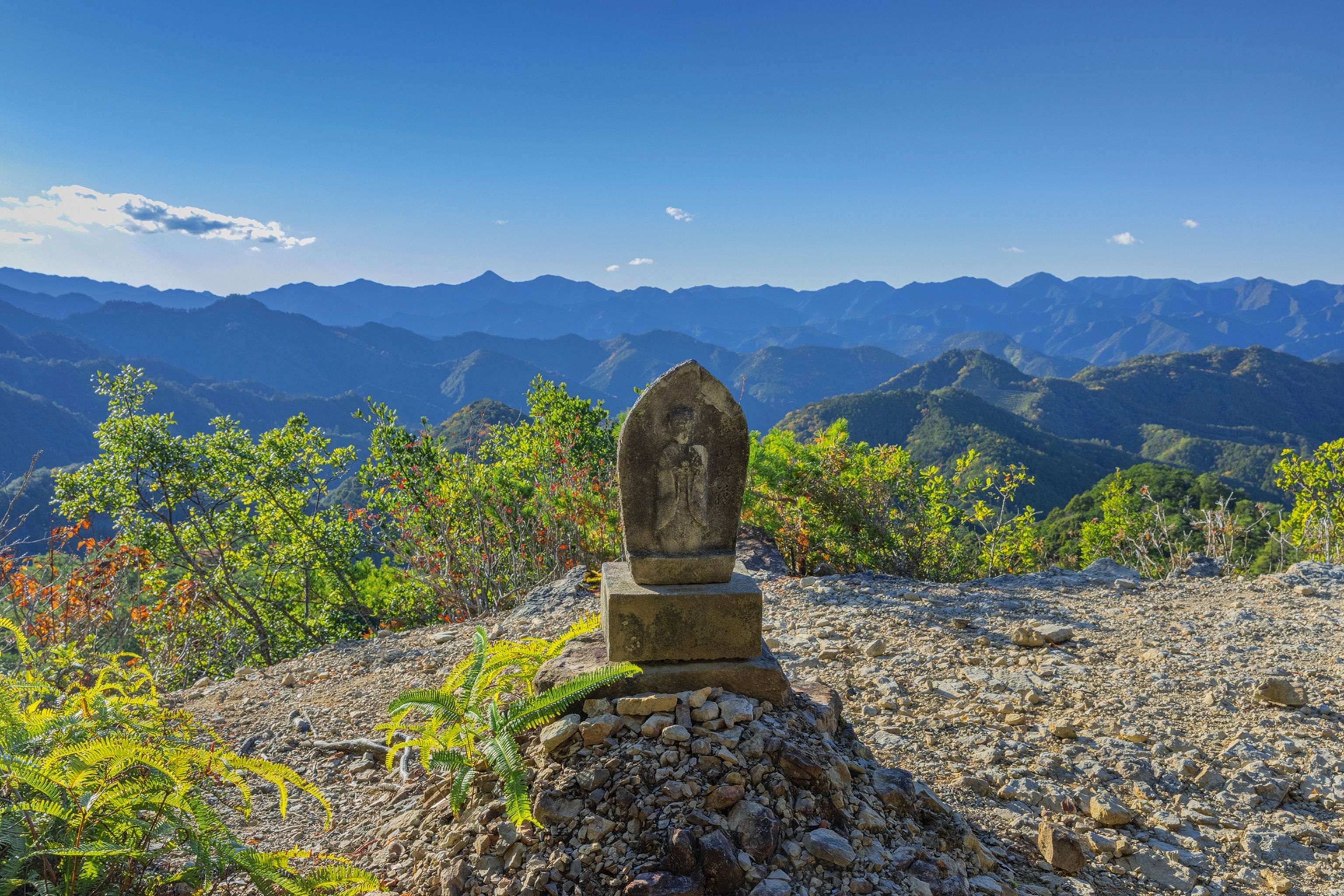 Stone statue standing on rocky terrain on top of a mountain viewpoint