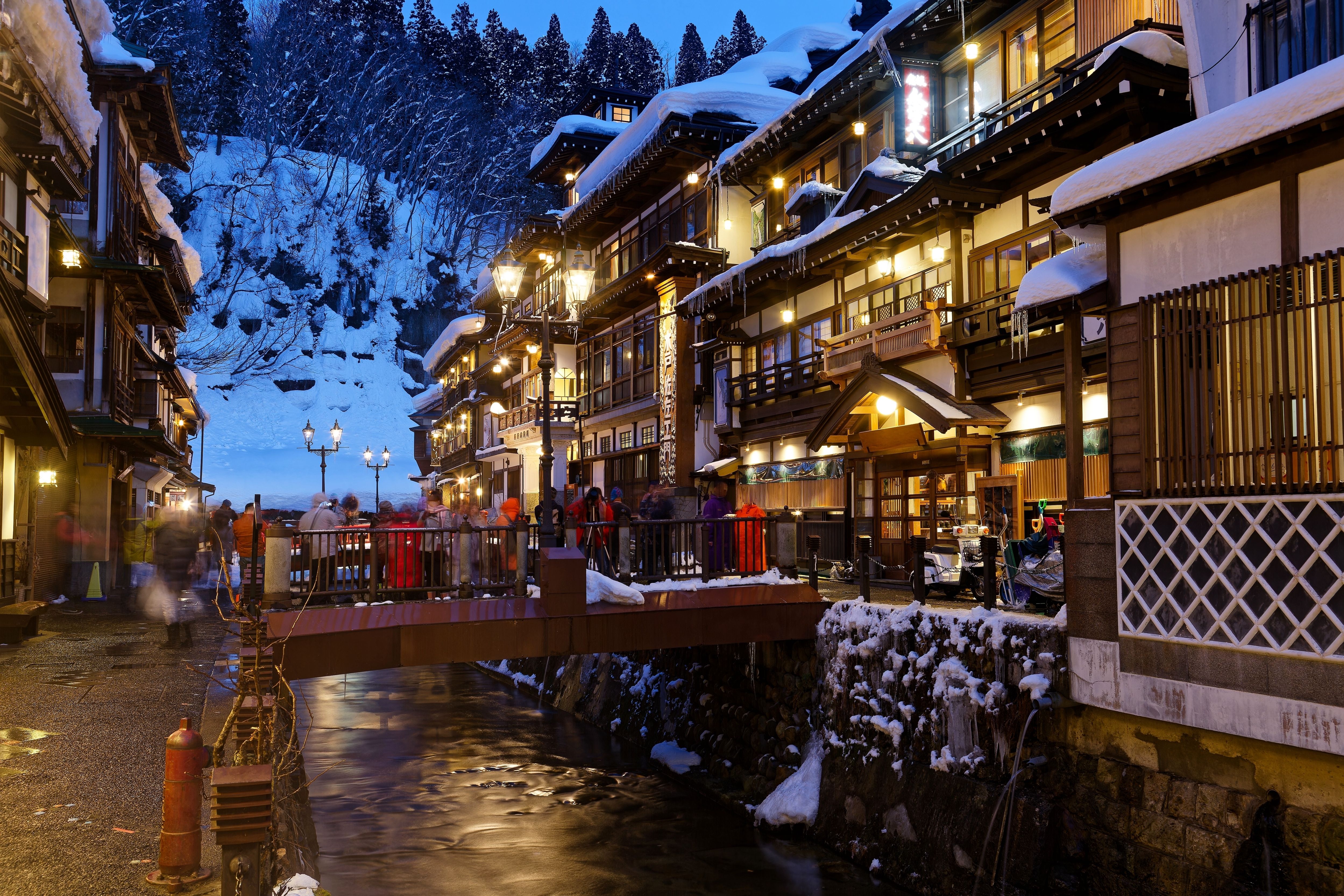 On a cold snowy winter night in Ginzan Onsen, tourists linger on a bridge flanked by old buildings