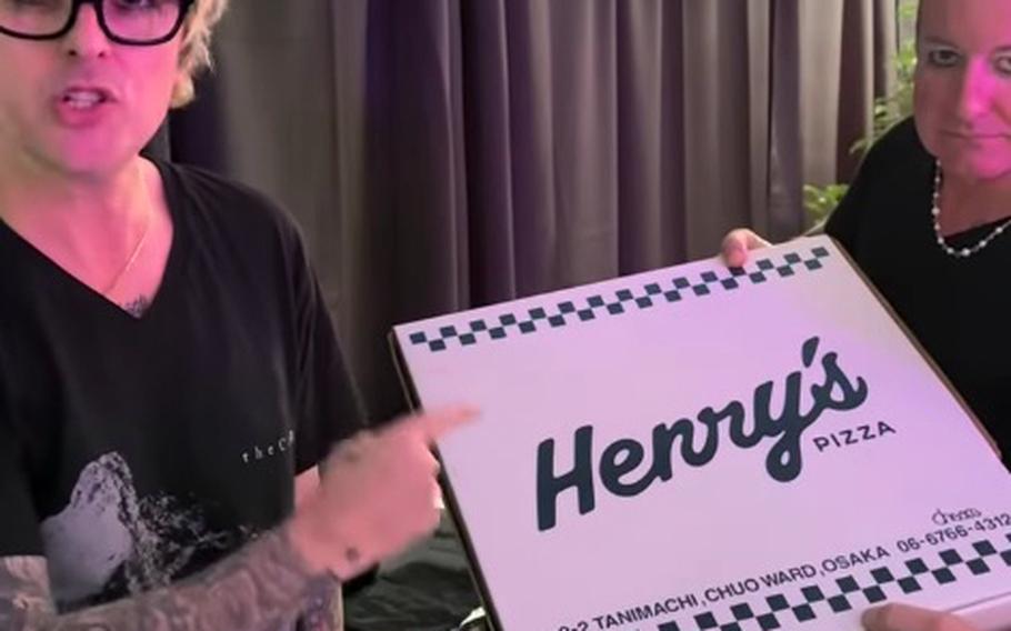 Two men hold a pizza box that says ‘Henry’s.’