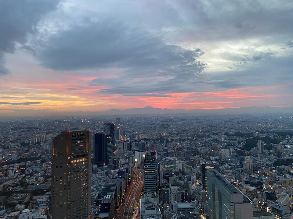 The sun sets over Tokyo skyscrapers on a cloudy day.