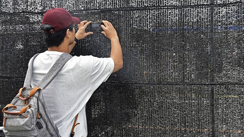 A visitor tries to take a photo through a hole on a black screen installed across from a convenience store in Fujikawaguchiko, Japan on 24 May 2024.