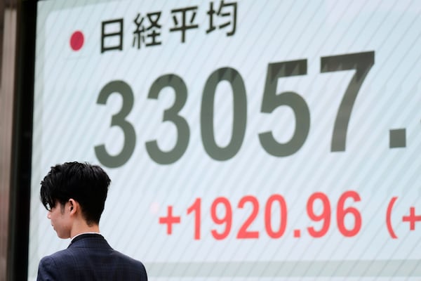 A man walks by monitors showing Japan's Nikkei 225 index at a securities firm in Tokyo, Tuesday, April 8, 2025. (AP Photo/Hiro Komae)