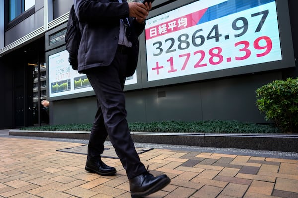 A man walk past monitors showing Japan's Nikkei 225 index at a securities firm in Tokyo, Tuesday, April 8, 2025. (AP Photo/Hiro Komae)
