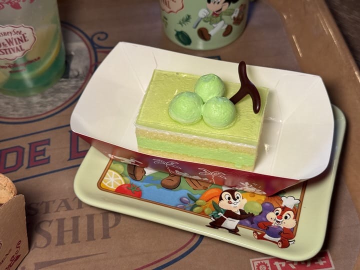A rectangular green layered dessert topped with three round green balls and a chocolate decoration, served on a themed tray featuring Disney's Chip and Dale characters, is a delightful treat at the 2025 Food and Wine Festival in Tokyo DisneySea.