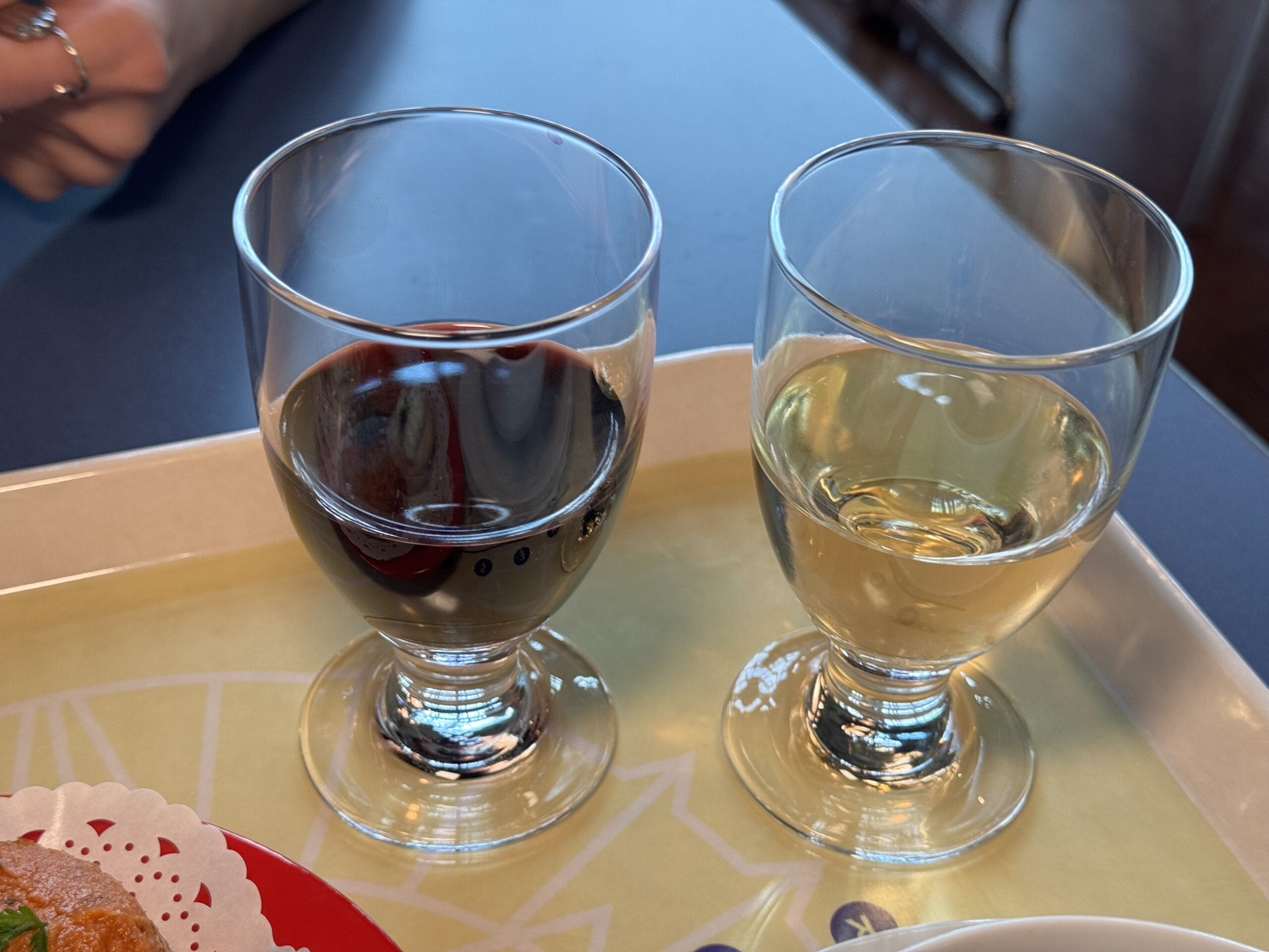 Two glasses, one with red wine and one with white wine, sit on a tray beside a plate of food—perfect for savoring the flavors of the 2025 Food and Wine Festival at Tokyo DisneySea.