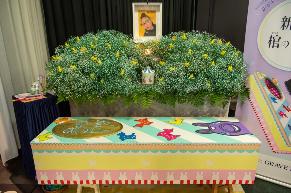 Hello, Death: Tokyo Event Gives Attendees a Chance to Die, Frankly Discuss The End Colorful painted coffin with someone's pictured above it and flowers in the background
