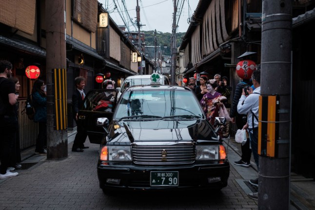 A group of tourists surround two maiko (apprentice geisha in