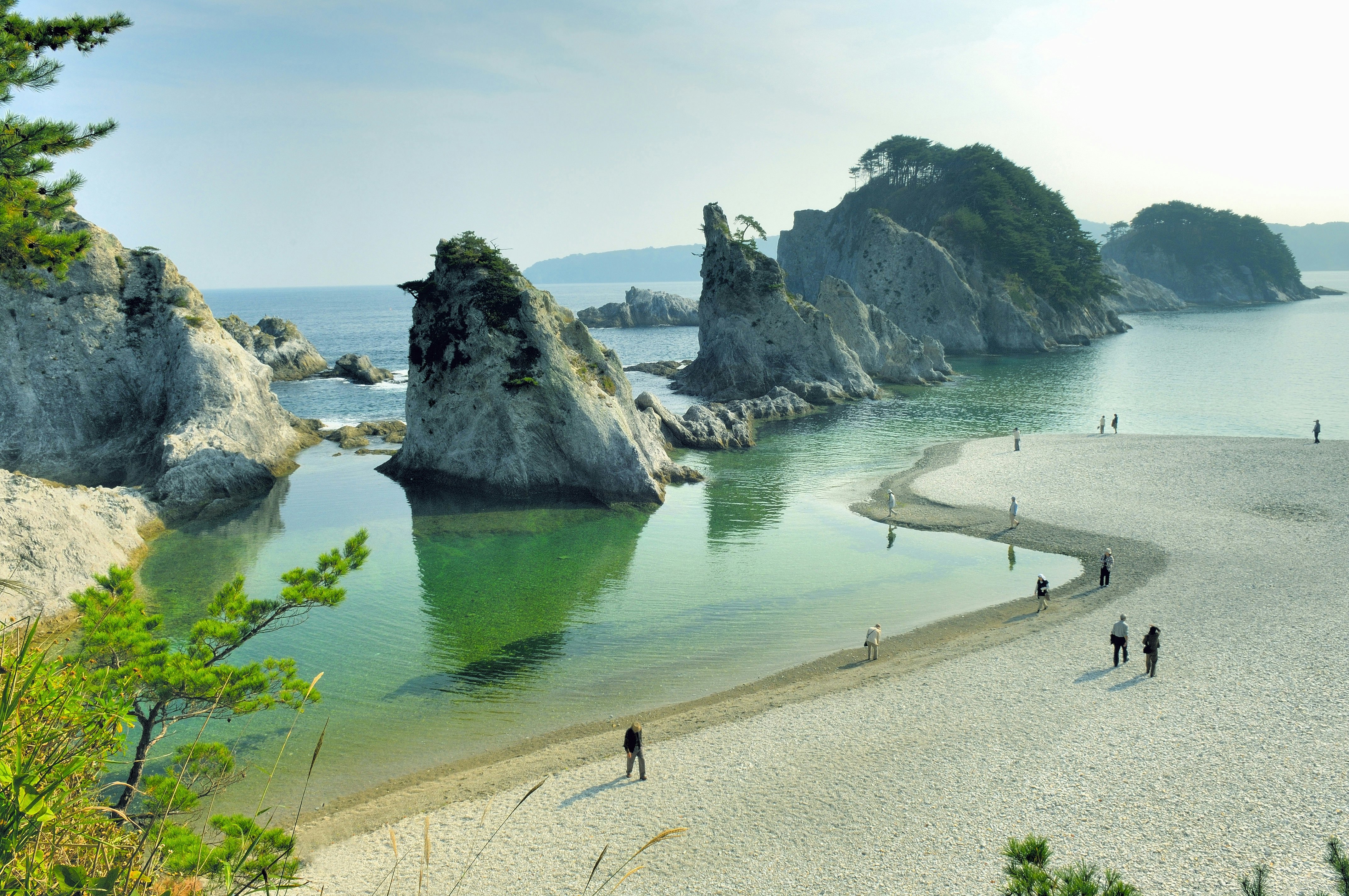 A series of rock stacks out beyond a sandy beach on a sunny day