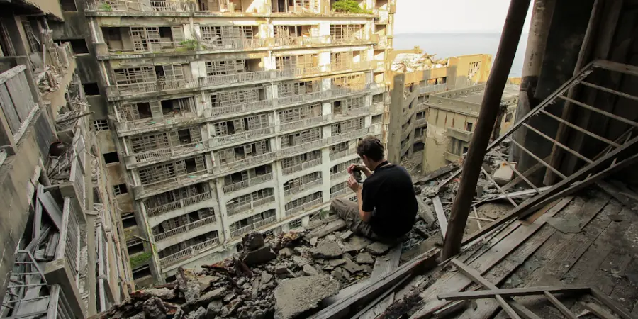 Tourist looking through his photos while sitting on a wrecked building in Hashima Island (Gunkanjima)