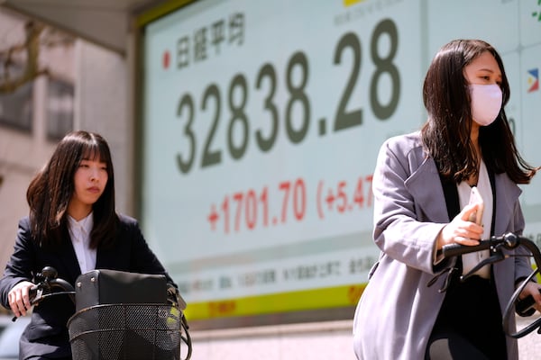 Women ride bicycles past monitors showing Japan's Nikkei 225 index at a securities firm in Tokyo, Tuesday, April 8, 2025. (AP Photo/Hiro Komae)