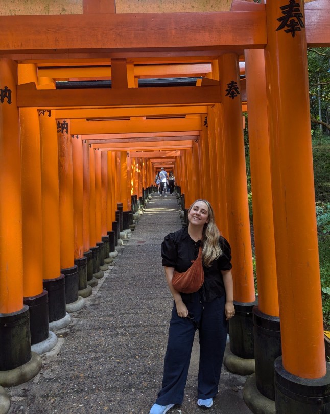 The writer smiling in front of the tori gates of Fushimi Inari shrine.