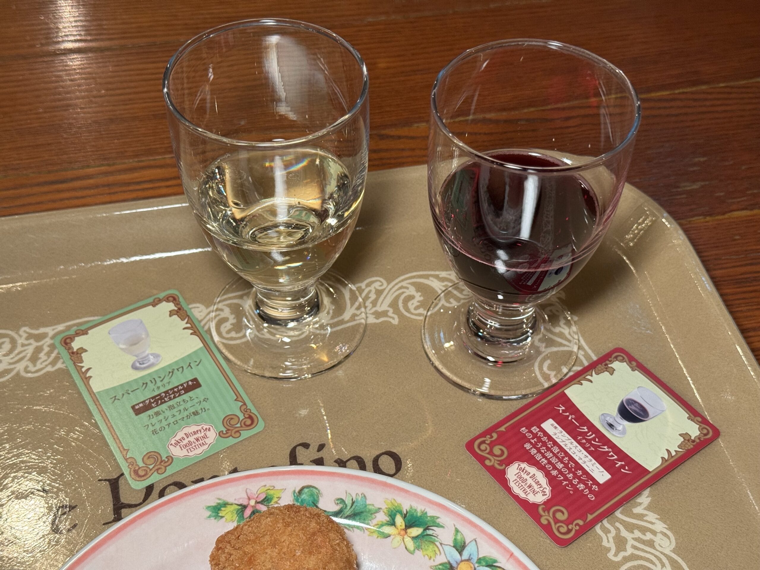 Two glasses of wine sit next to tasting cards and food at the 2025 Tokyo DisneySea Food and Wine Festival.
