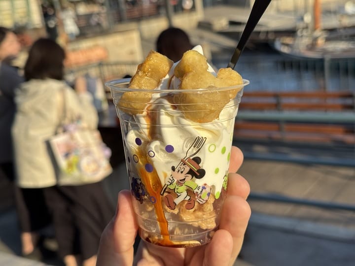 A hand holds caramel sundae with tater tots in a Mickey Mouse cup at Tokyo DisneySea’s waterfront during the 2025 festival.