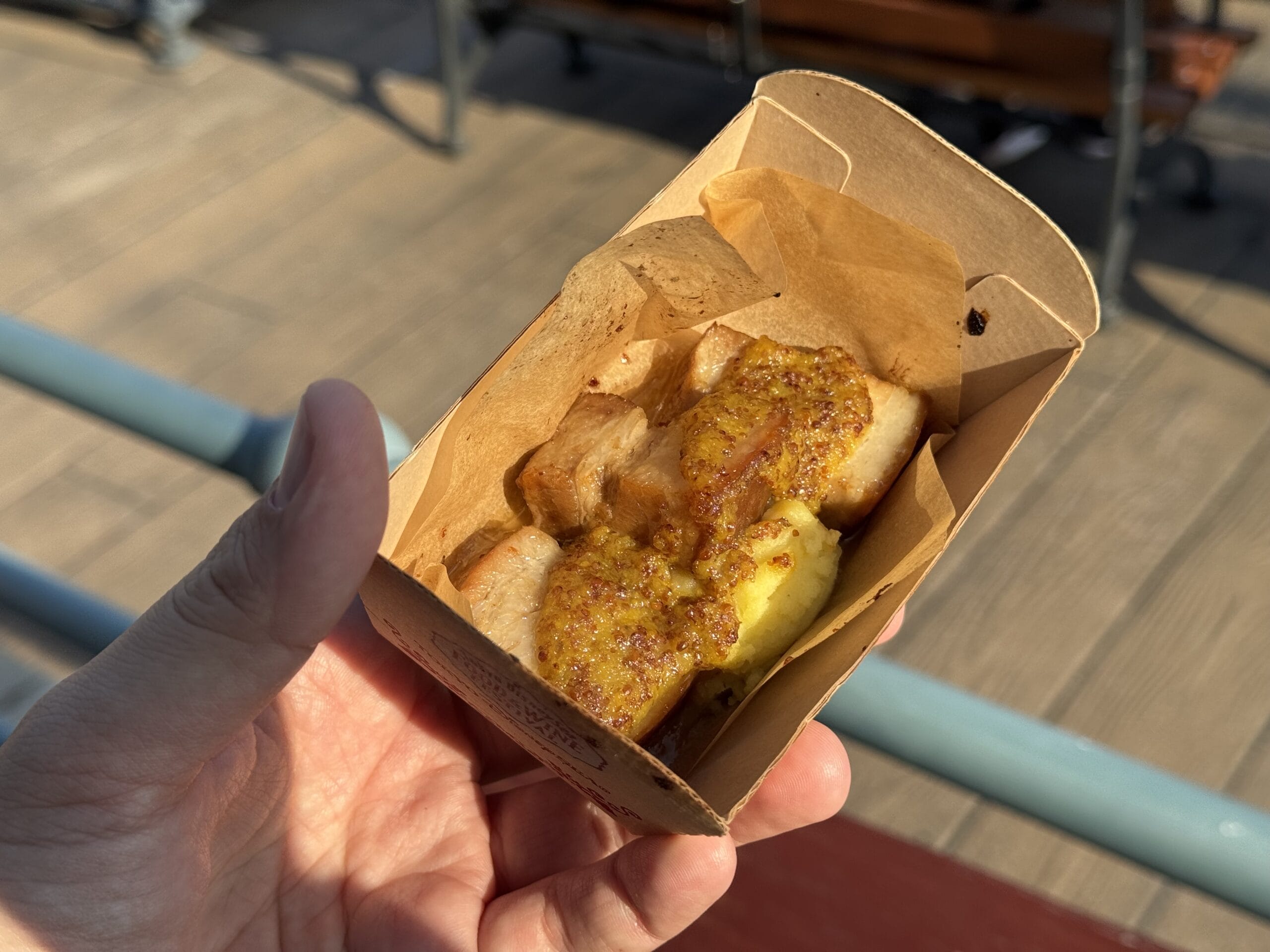 A hand holds grilled skewered chicken with yellow sauce at the 2025 Food and Wine Festival, Tokyo DisneySea.