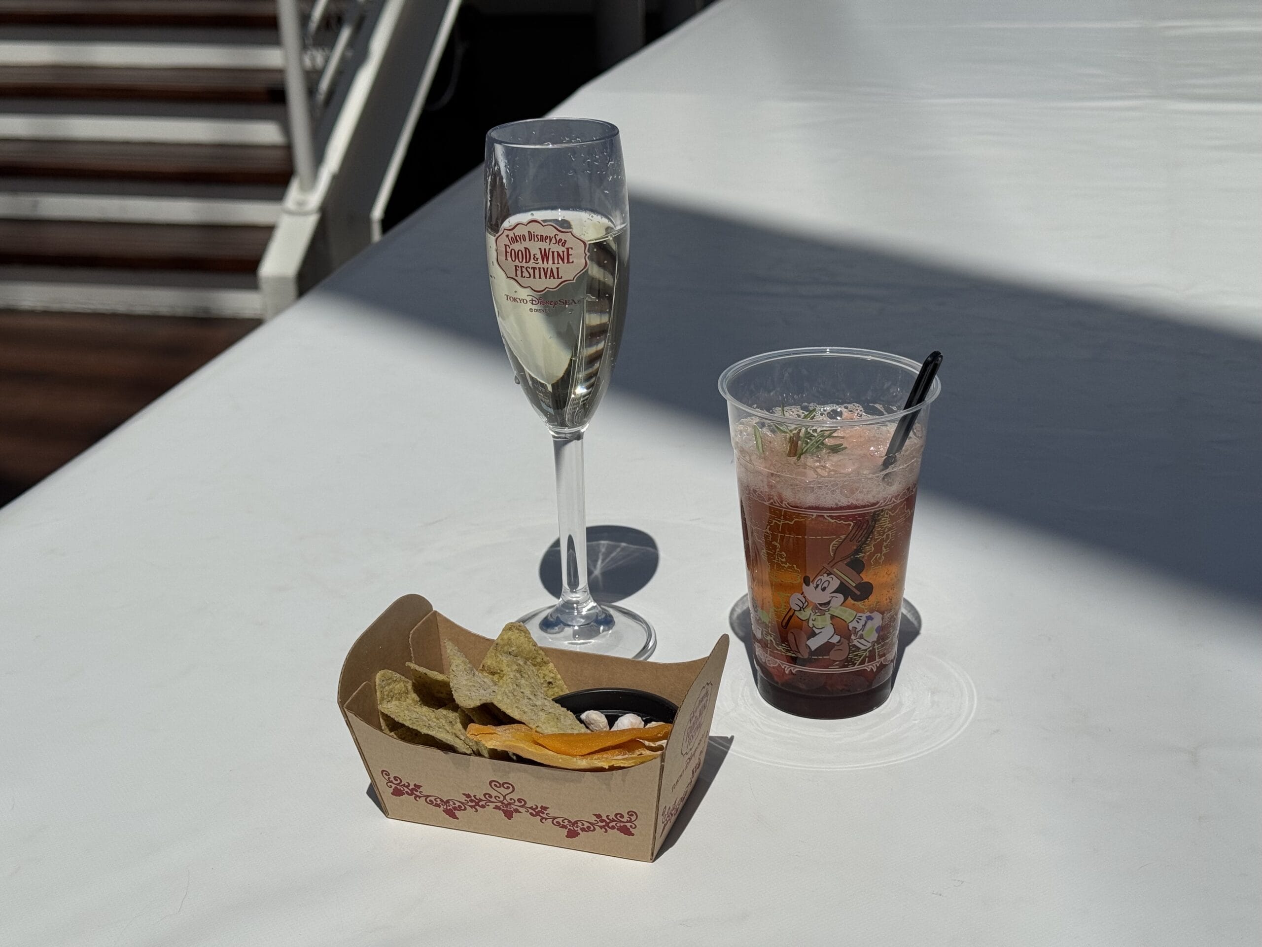 A glass of wine, a pink drink in a Mickey cup, and chips with dip at Tokyo DisneySea’s Food and Wine Festival 2025.