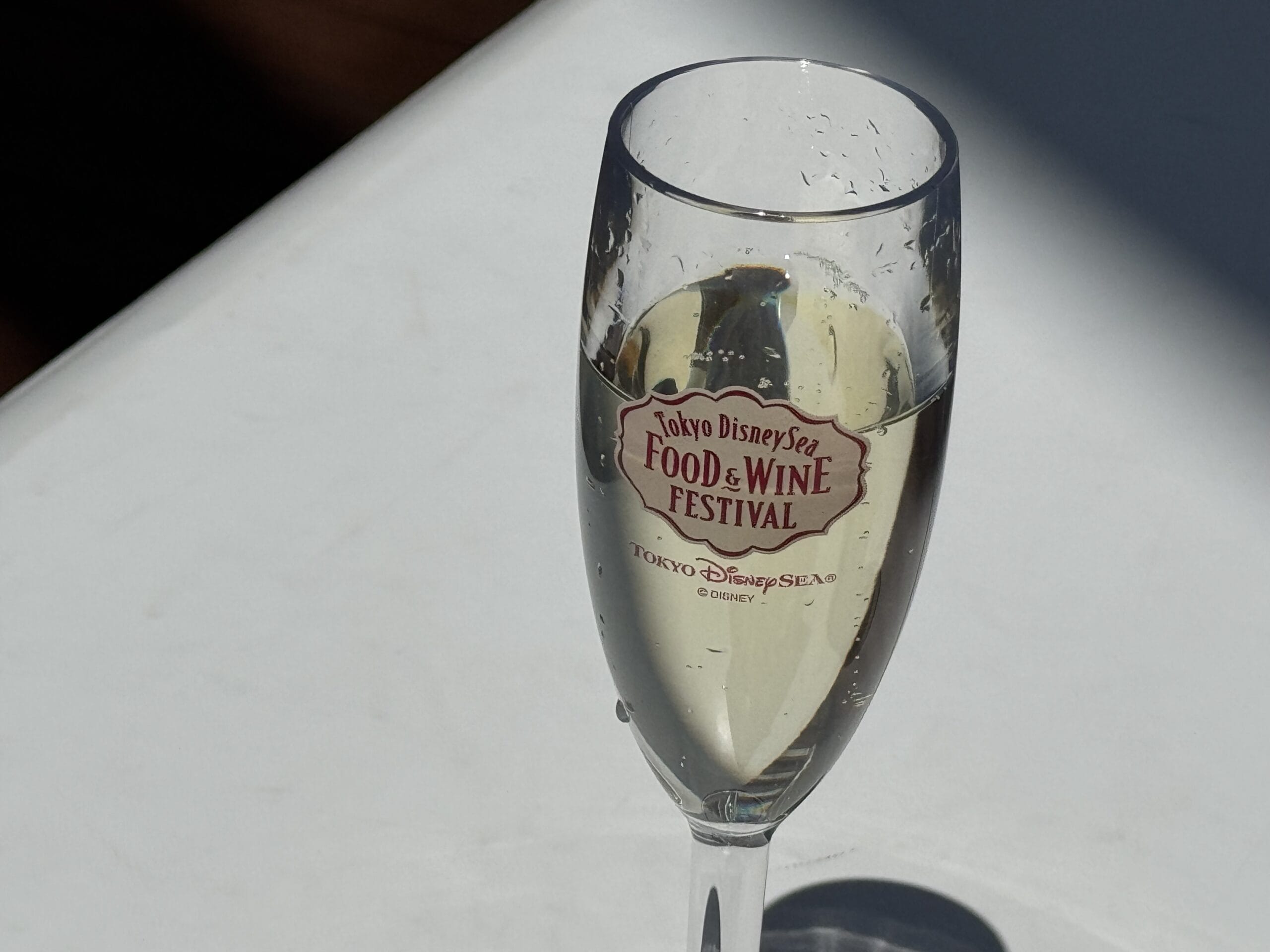 A champagne glass from the 2025 Tokyo DisneySea Food and Wine Festival, filled with a light sparkling drink.