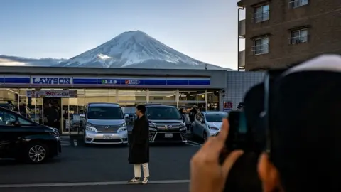 Getty Images An image showing a photo being taken of a person standing in front of a Lawson shop, with Mount Fuji in the background
