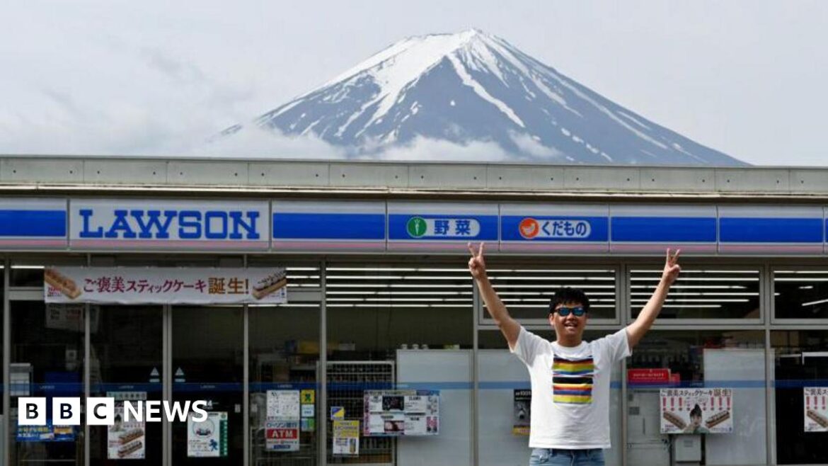 A tourist poses for photograph with Mount Fuji in front of a Lawson convenience store