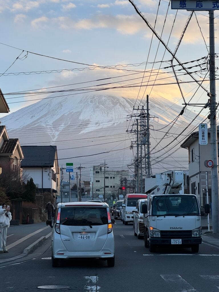Power lines crisscross the sky in front of a view of Mt. Fuji in a snowy Japanese town.