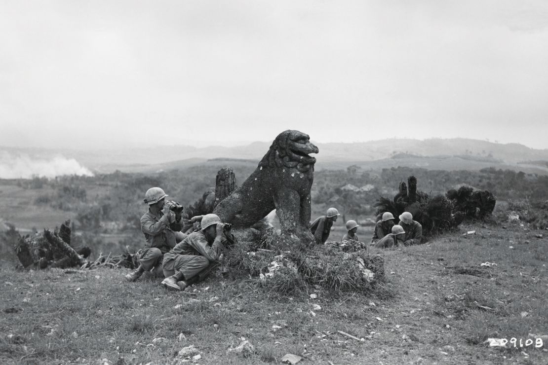 Soldiers from the US Army's 7th Infantry Division, take cover around the Tomori Stone Lion as they observe Japanese action on the ridge ahead during the World War II Battle of Okinawa. The statue survived the battle and sits on the same site today and can be seen by visitors to the island.