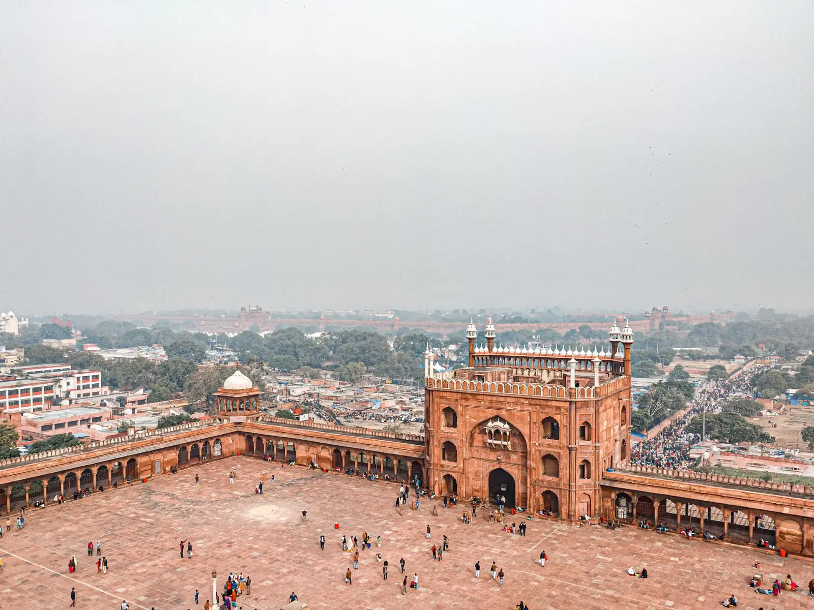 Aerial view of Jama Masjid courtyard in Delhi, India, with visitors exploring the historic site on a hazy day.