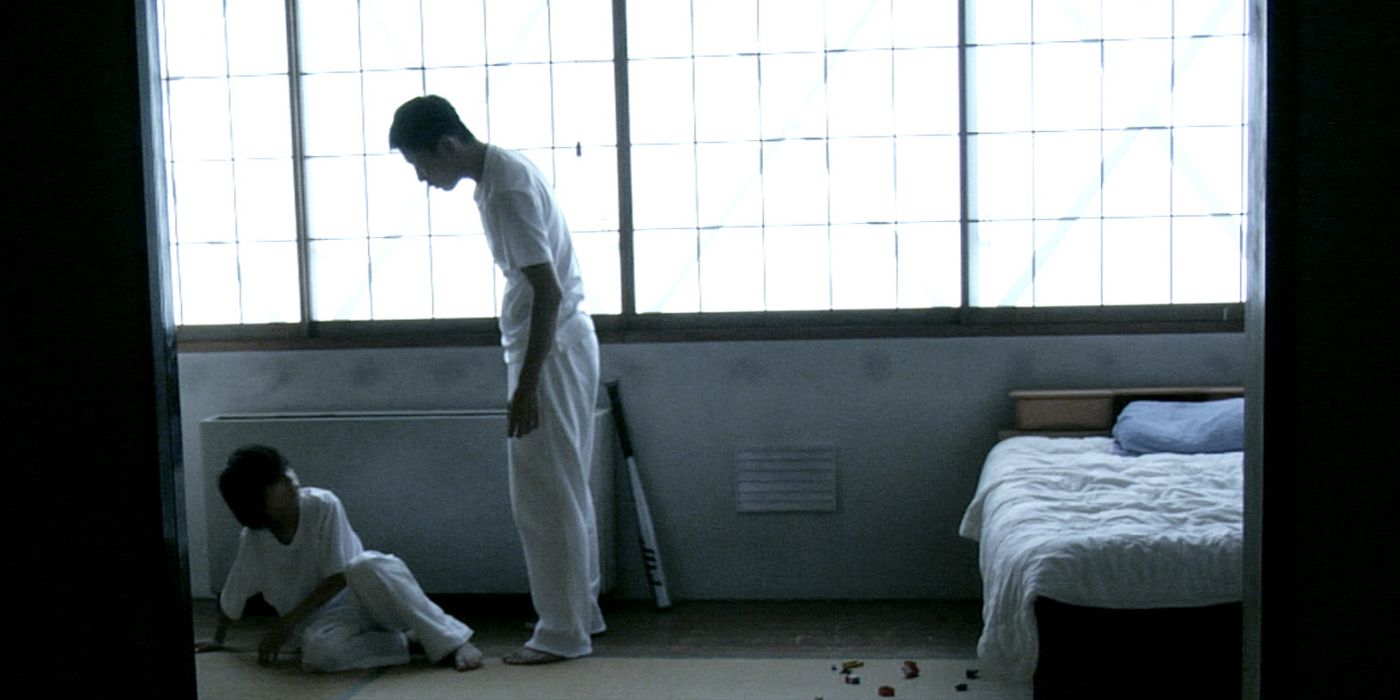 A man standing over his son while the child is sitting on the floor in Mimicry Freaks