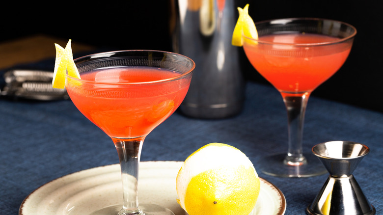 A bright orange cocktail in a coupe glass garnished with lemon peel.