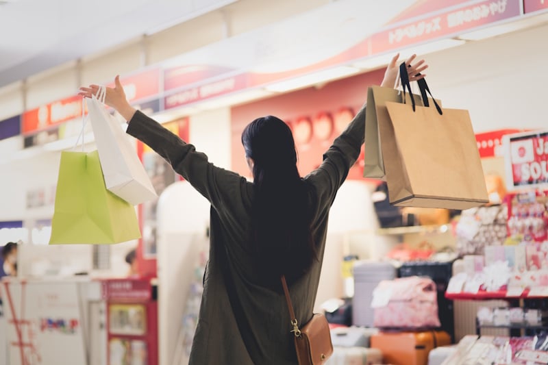 Woman looking away from the camera and holding up her hands in celebration with shopping bags dangling from each