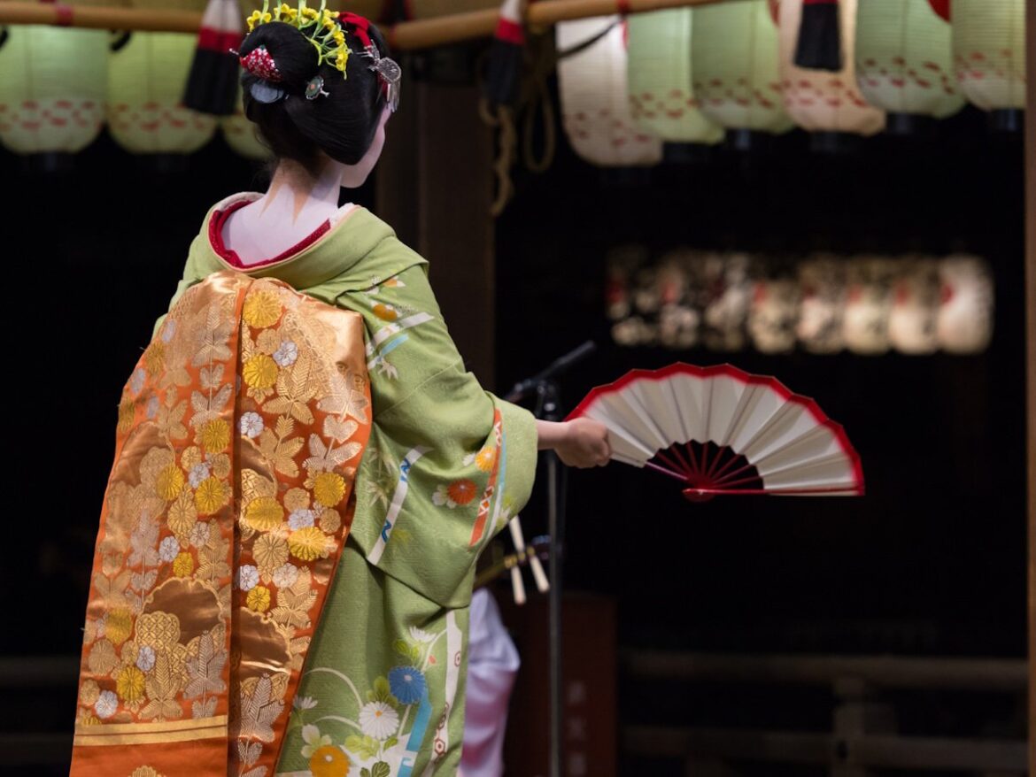 Maiko (apprentice geisha) shot from the back holding a fan in her right hand