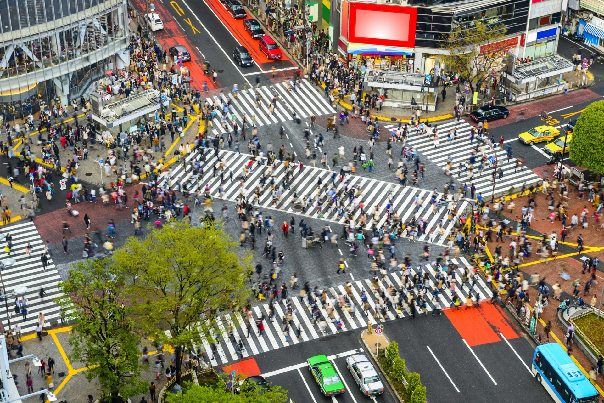 An overhead view of people on the crosswalks of the Shibuya Crossing with traffic stopped in all directions.