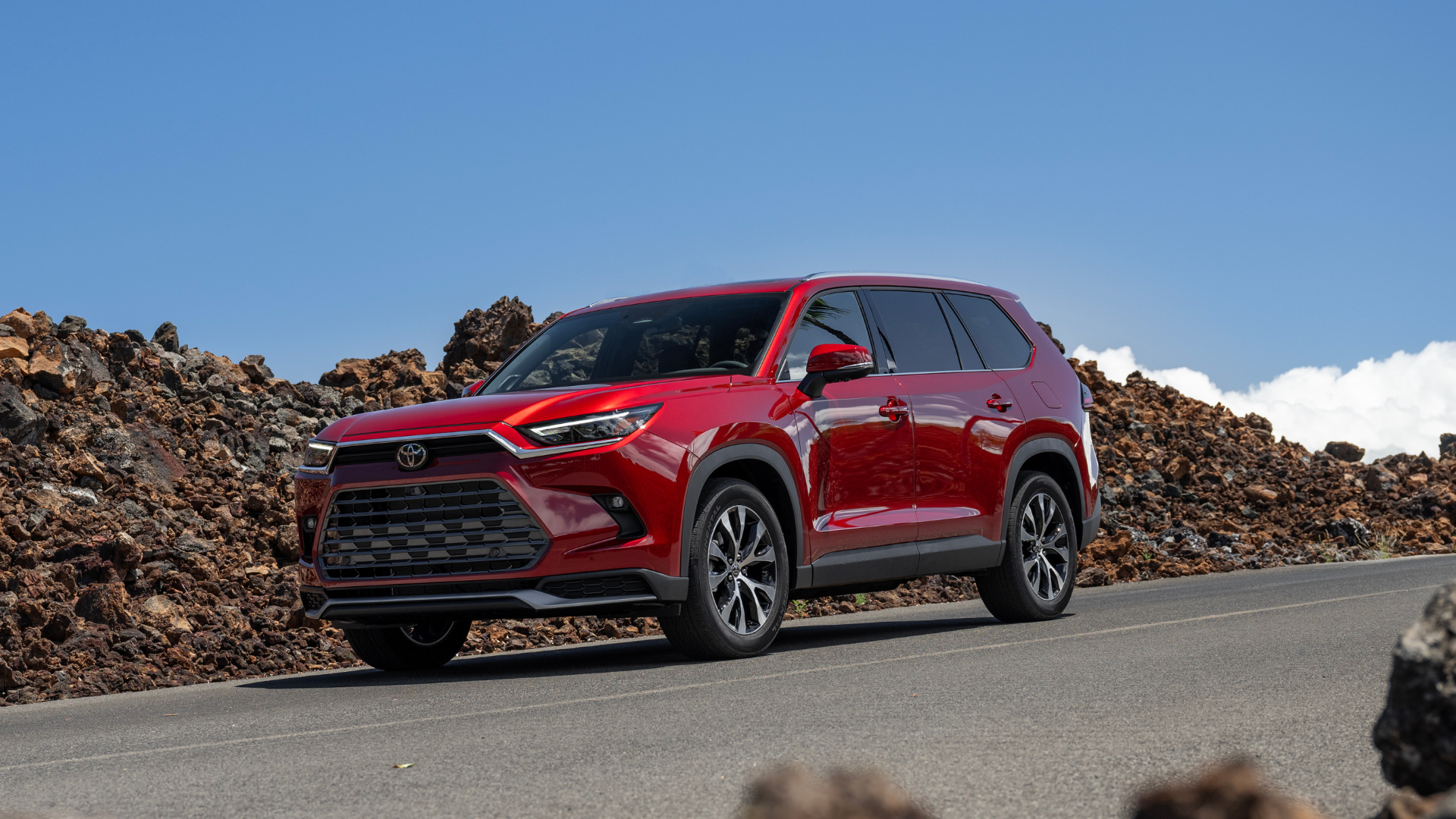 2024 Toyota Grand Highlander Hybrid in red driving along road