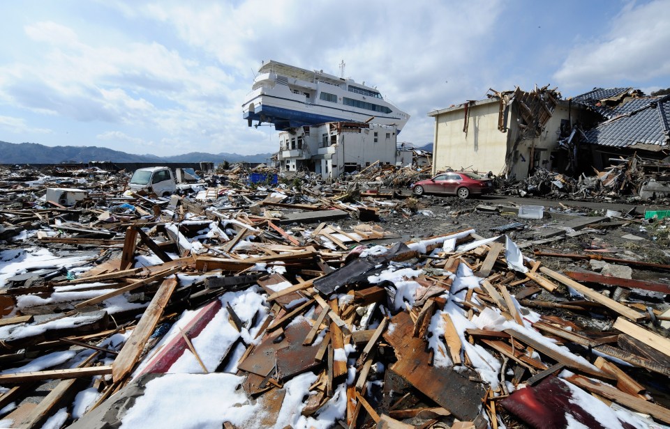 A cruise ship rests atop a damaged building amidst the debris of a tsunami.