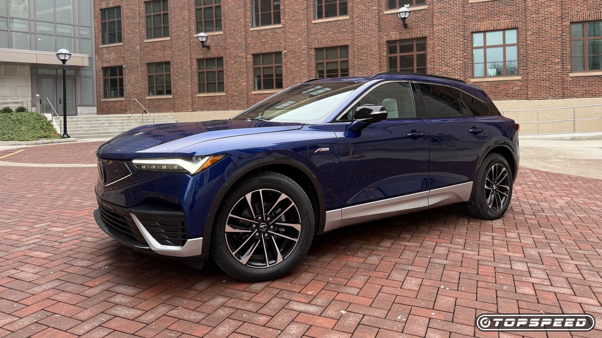 Static front three-quarters photo of a blue 2025 Acura ZDX A-Spec with a building in the background