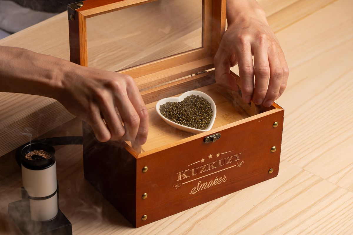 A dish of caviar being smoked in a small wooden box.