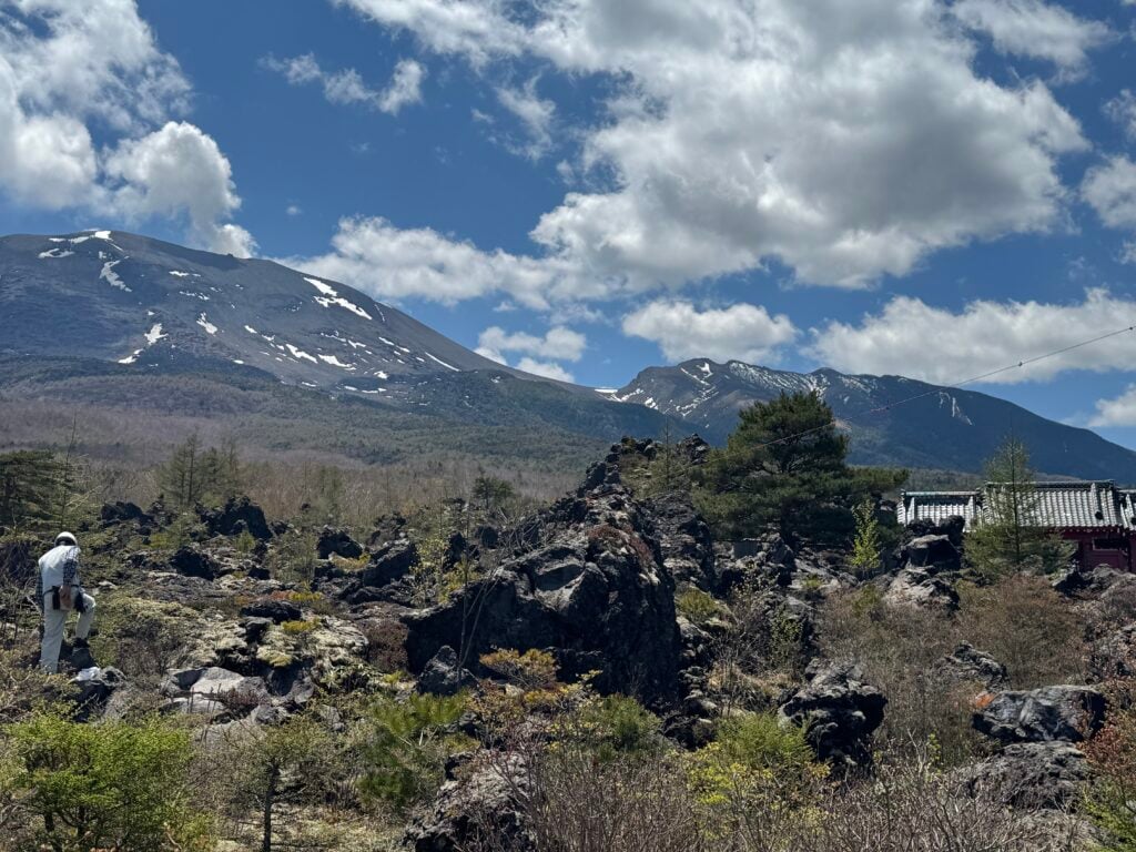 Volcanic and crags in front of a mountain range, with a blue sky filled with white clouds.