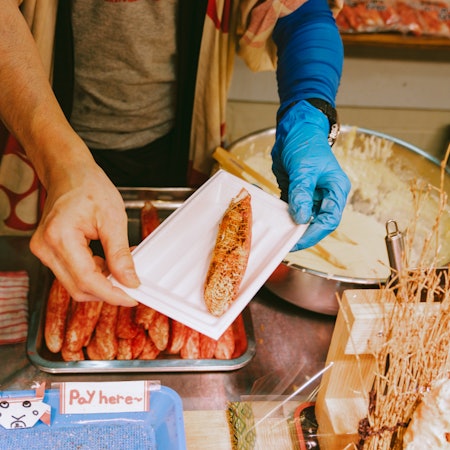 A person hands a customer food at a market stall 
