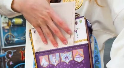 A person places a folded napkin into a decorative Disneyland purple insulated cooler bag with fantasy-themed designs.