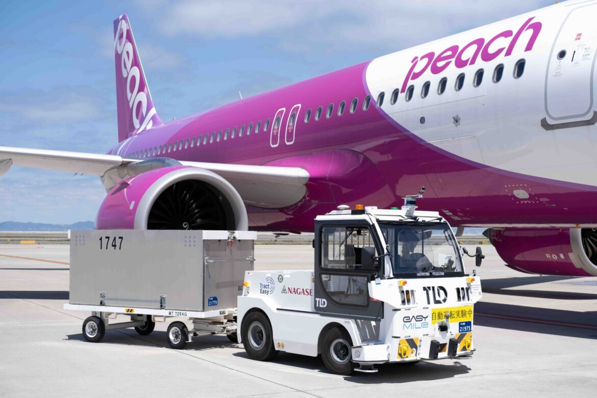 A driverless baggage towing vehicle from TLD and EasyMile operates autonomously on the tarmac, positioned beside a Peach Aviation aircraft at an airport.
