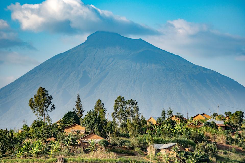 Houses within a small village are dwarfed by the looming presence of a volcanic mountain, Rwanda,