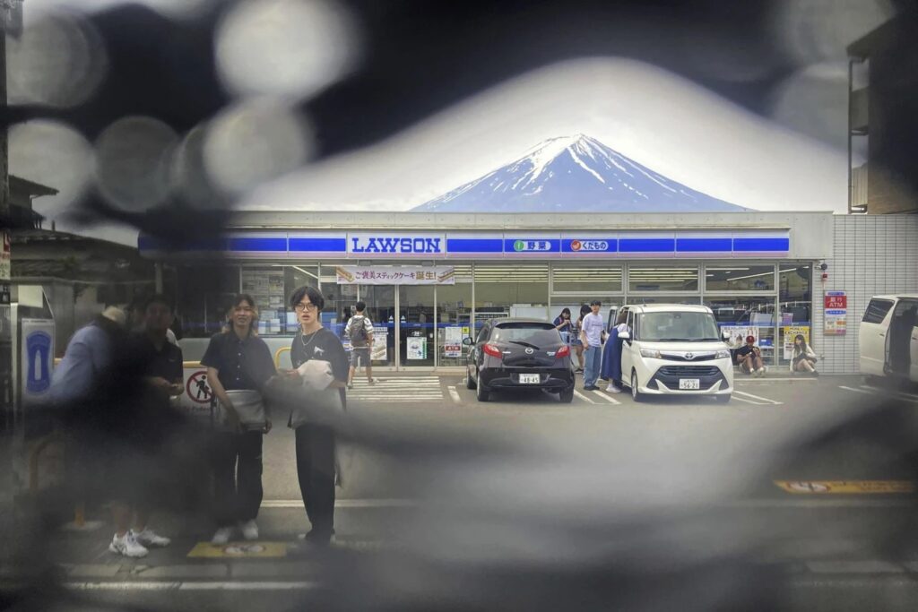 Mt. Fuji is seen through a hole on a black screen installed across from a convenience store in Fujikawaguchiko town, Yamanashi prefecture, central Japan on May 24, 2024. The town that erected the huge black screen last week in an attempt to stop tourists from snapping photos of Mount Fuji and overcrowding the area has discovered holes in the screen and is working to repair them, officials said Tuesday.