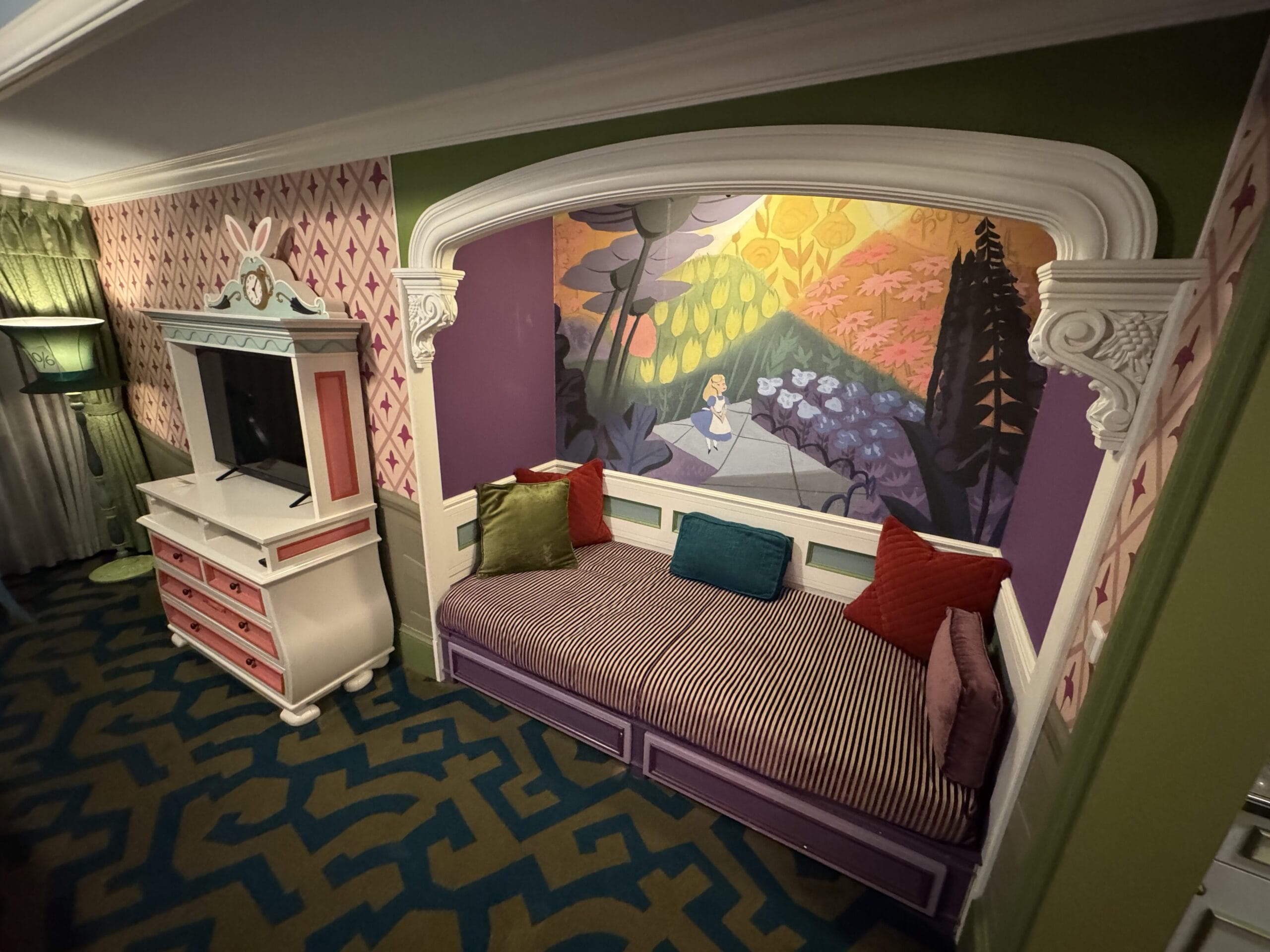 A whimsical Alice in Wonderland Hotel Room with a daybed, colorful pillows, and a mural above the bed.